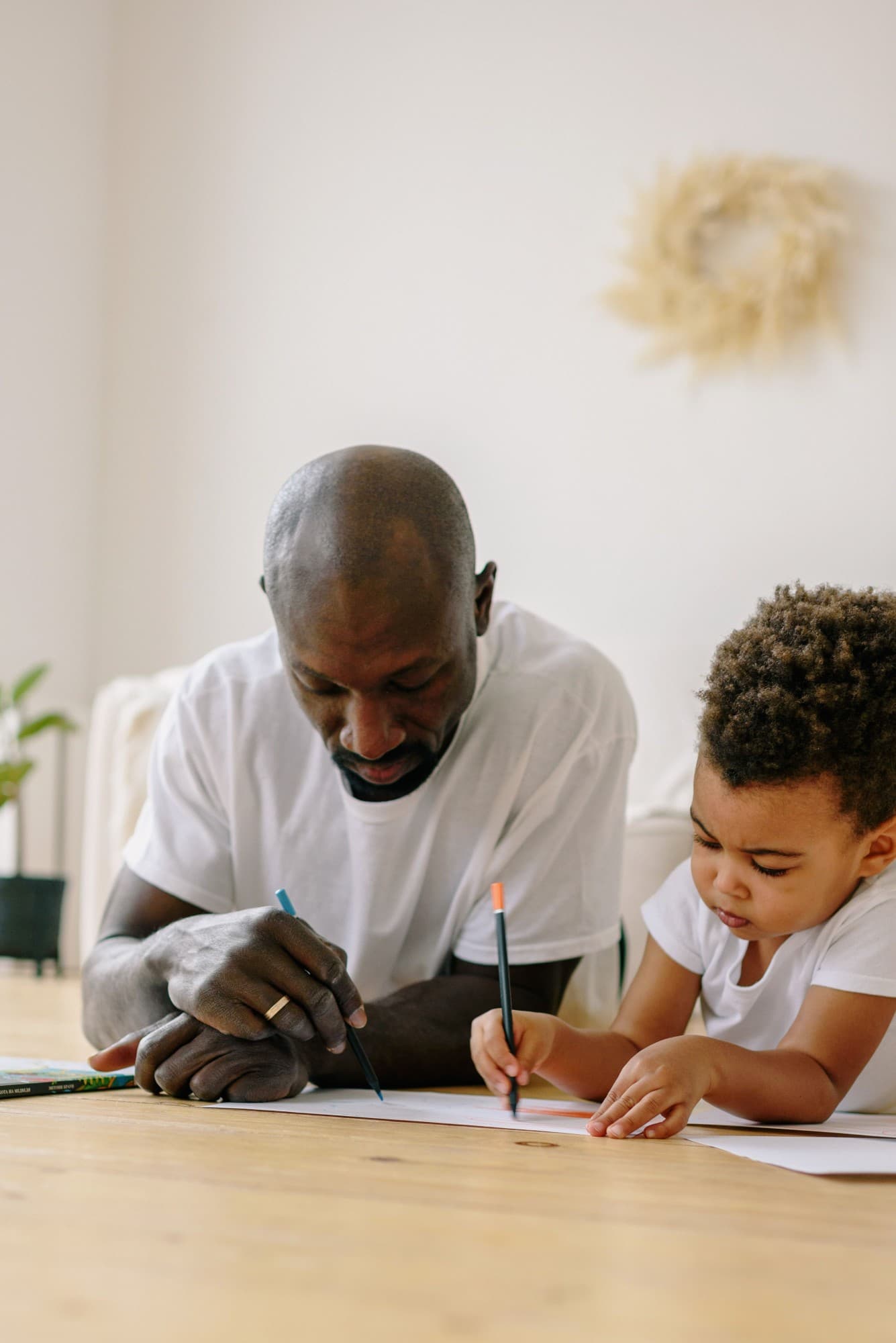 An adult and a young child drawing side by side with coloured pencils
