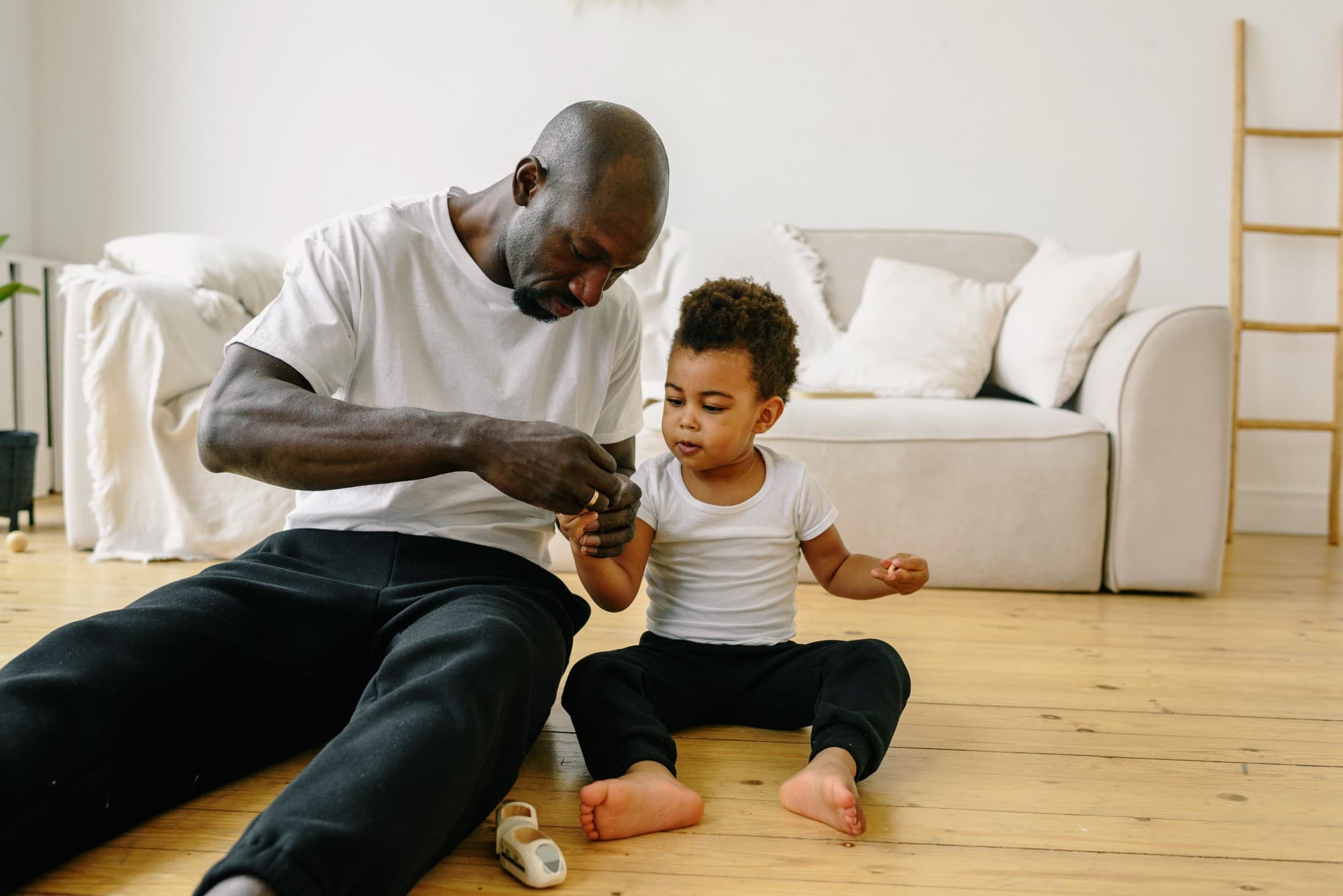 A father sitting on the floor with his toddler, helping him with a small toy