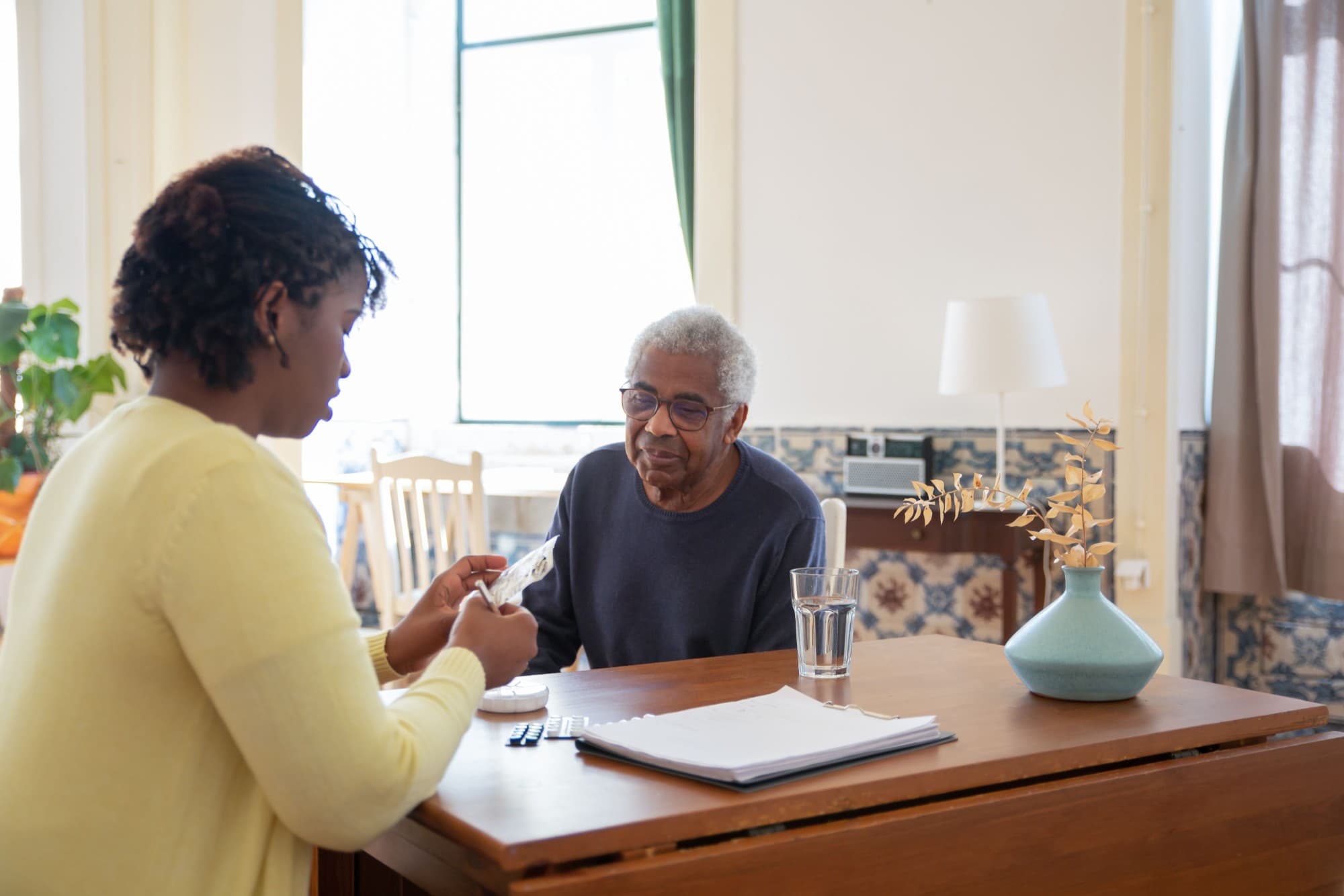 A therapist going through medication and notes with an older man at his dining table